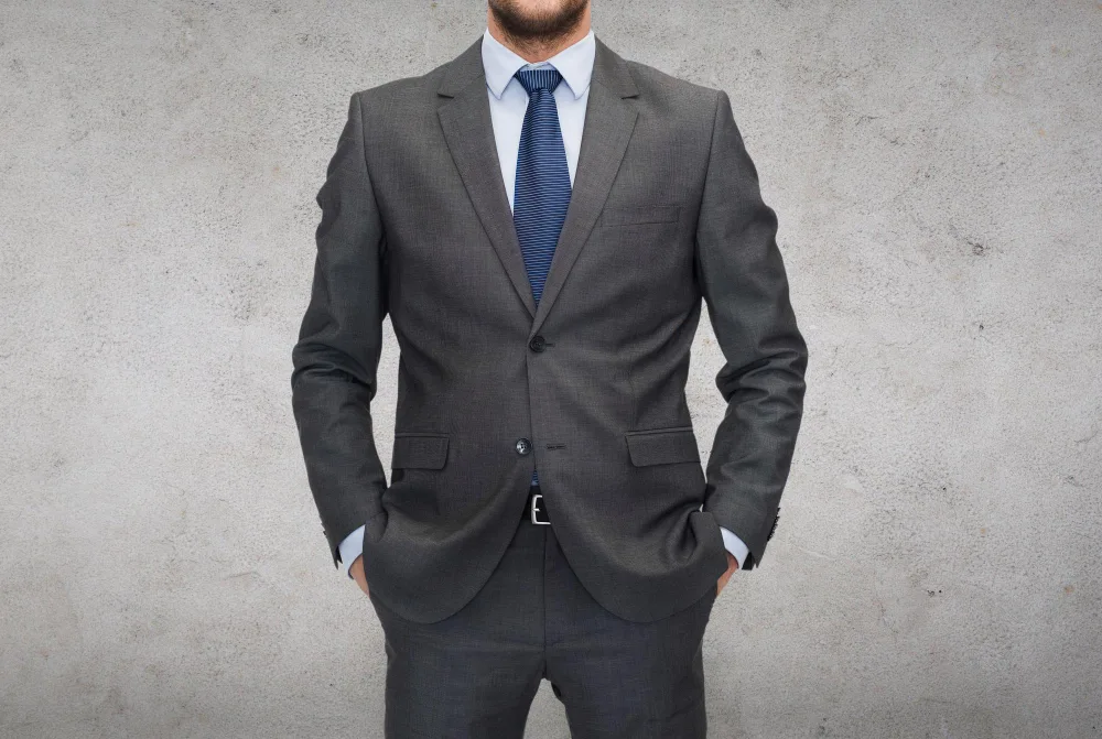 Man in a Charcoal Grey suit against a concrete background
